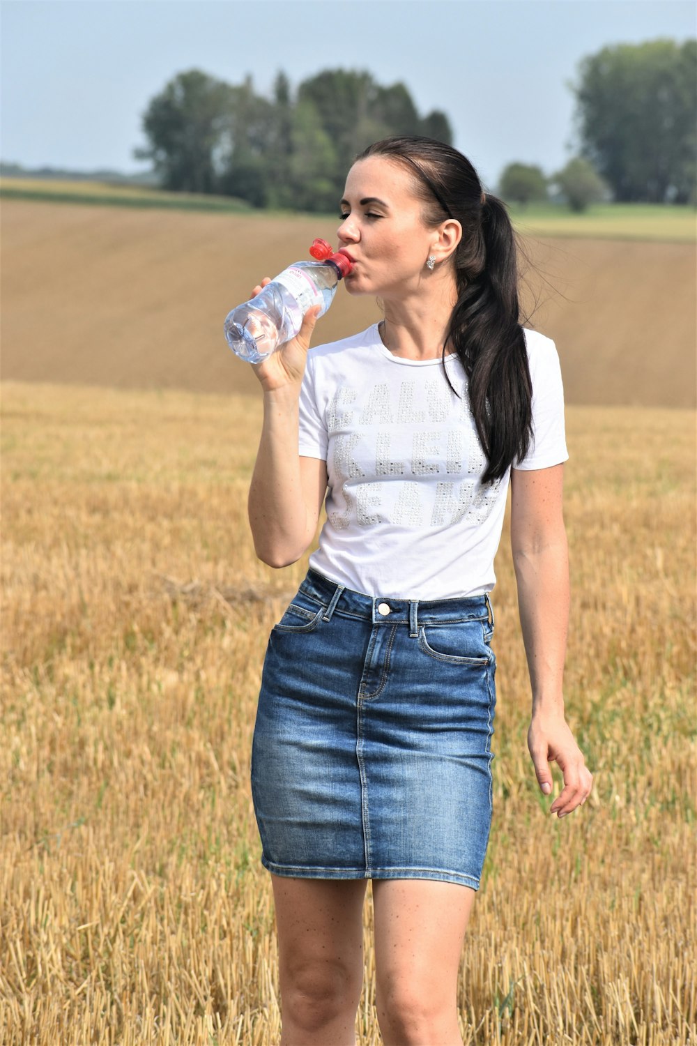 a woman standing in a field drinking from a bottle