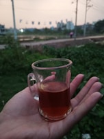 A hand holding a cup of tea against a backdrop of city skyline at sunrise.