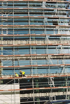 A modern building under construction with scaffolding and workers in safety gear.