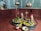 A sacred space adorned with vibrant marigold and rose flowers surrounding stone deities, including a Shivlinga. Metallic vessels hang above and a brass lamp stands lit in the center, casting a serene glow. A small altar with idols decorated with flowers is visible in the background.