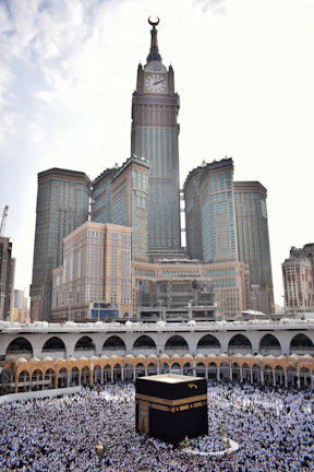 A serene view of the Grand Mosque in Macca, bustling with pilgrims under a clear blue sky.