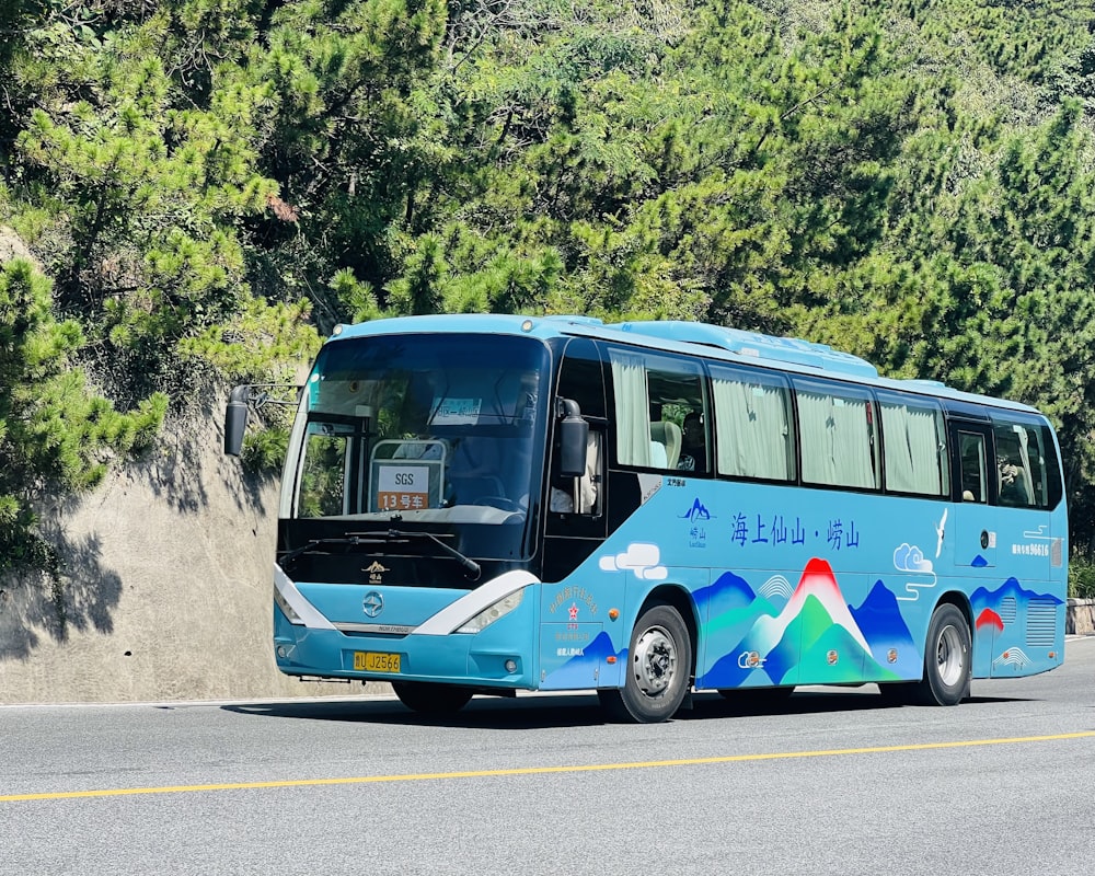 a blue bus driving down a road next to a forest