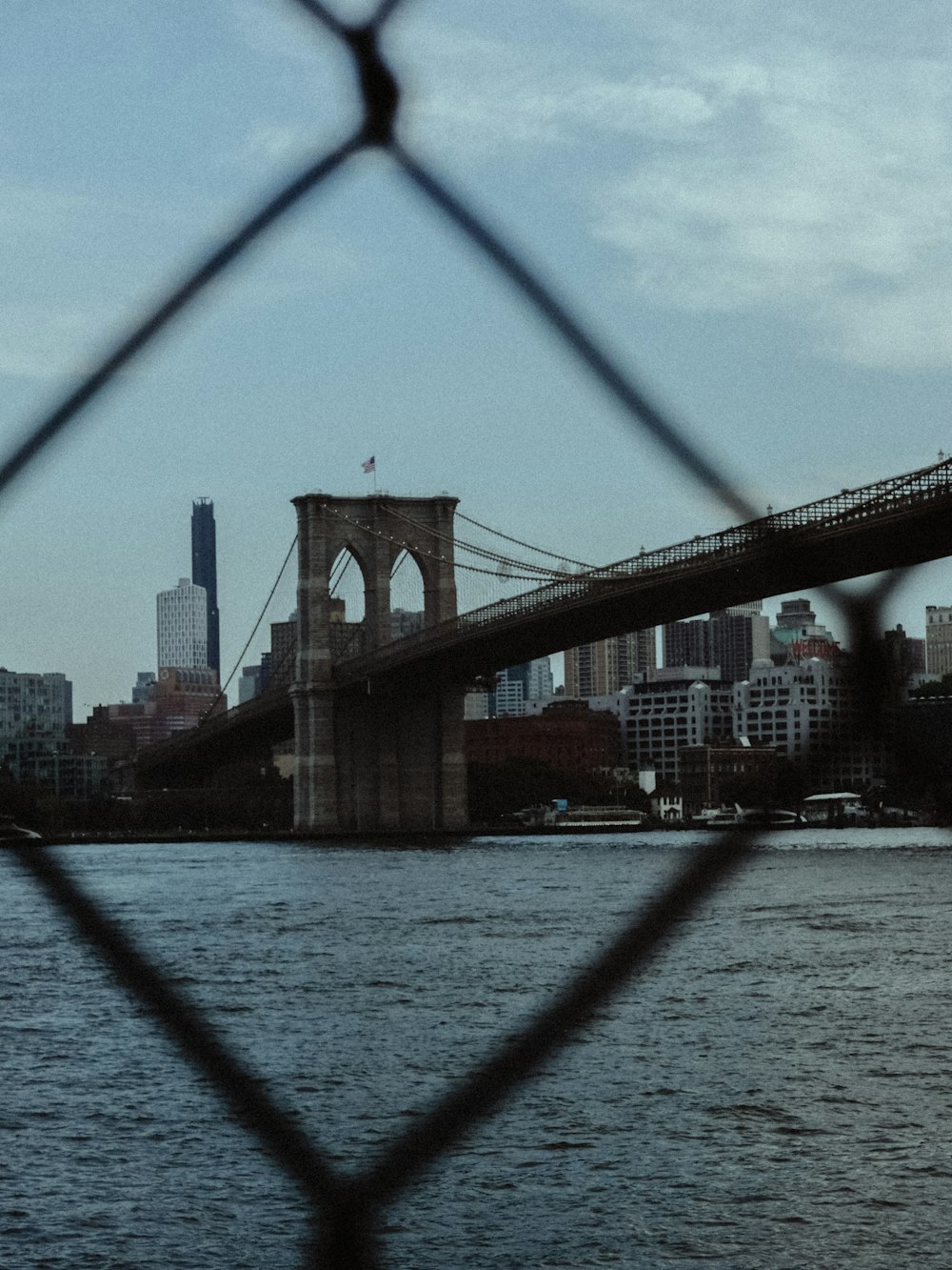 a view of the brooklyn bridge through a chain link fence
