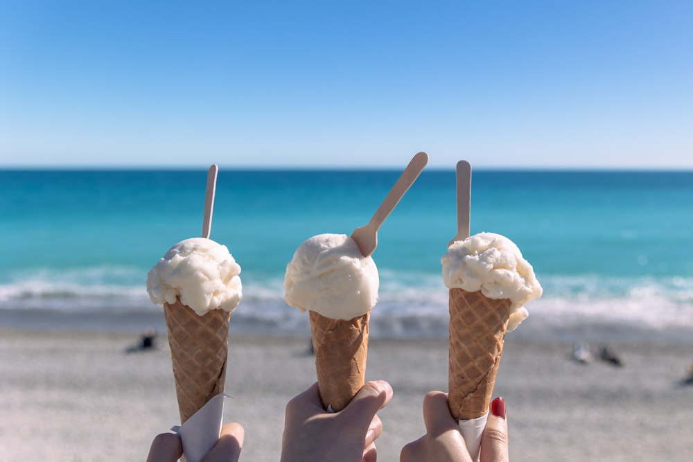 three people holding ice cream cones on a beach