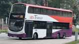 A double-decker bus with a red, white, and purple color scheme featuring the logo 'SBS Transit' on the side. The destination sign on the front of the bus displays route number 513. The bus is parked on a city street with greenery and buildings visible in the background.