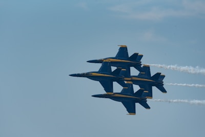 A formation of four fighter jets flying closely together in the sky with contrails trailing behind them. The aircraft are sleek and have a distinctive navy blue and yellow color scheme.
