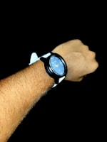 Wrist shot of the watch worn with a sleek black suit, the deep navy strap blending seamlessly with the jet black gradient background.