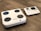 A digital body composition analyzer featuring a square platform with four circular metal sensors and an attached console with a display and various buttons. Both components are white with a sleek, modern design, placed on a wooden floor.