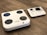 A digital body composition analyzer featuring a square platform with four circular metal sensors and an attached console with a display and various buttons. Both components are white with a sleek, modern design, placed on a wooden floor.
