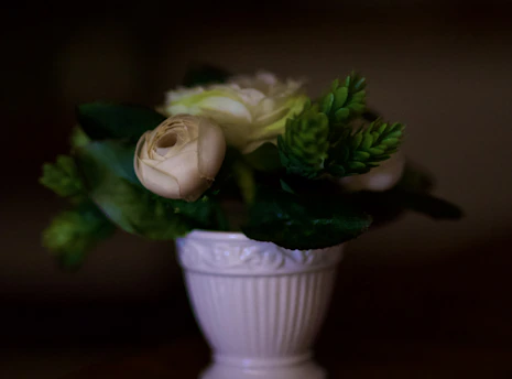 A delicate bouquet of pastel pink roses elegantly arranged in a white ceramic vase on a minimalist cream background.