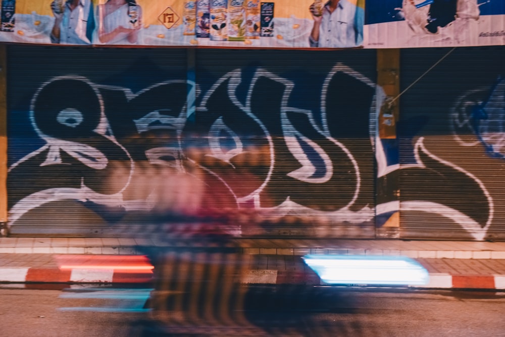 a man riding a motorcycle past a graffiti covered building