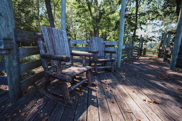 A rustic wooden rocking chair set on a sunlit patio surrounded by greenery.