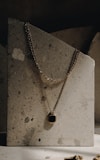 Minimalist gold necklace with a small pendant displayed on a white marble surface