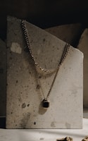 Minimalist gold necklace resting on a smooth marble slab with warm lighting.