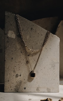 Minimalist gold necklace resting on a smooth marble slab with warm lighting.