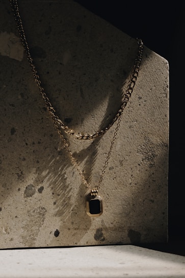 Close-up of a sleek gold necklace resting on a textured concrete surface, capturing urban elegance.