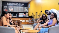 A group of students laughing and chatting over coffee at the shop.