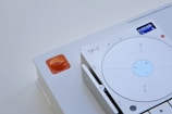 A close-up of a modern electronic device featuring a circular dial with a small digital display in the top right, showing the time 0:00:55 and a day indicator. The device is predominantly white with minimalist design elements and the letters 'TP-7' are visible near the dial. An orange, semi-transparent button or indicator is positioned on the left side of the image.