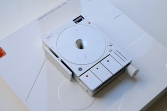 A sleek, modern device with a minimalist design featuring a circular dial and several buttons. The device is labeled 'TP-7' and includes a digital screen displaying numbers and symbols. The overall aesthetic is clean and futuristic, with a light gray color scheme and rounded edges.