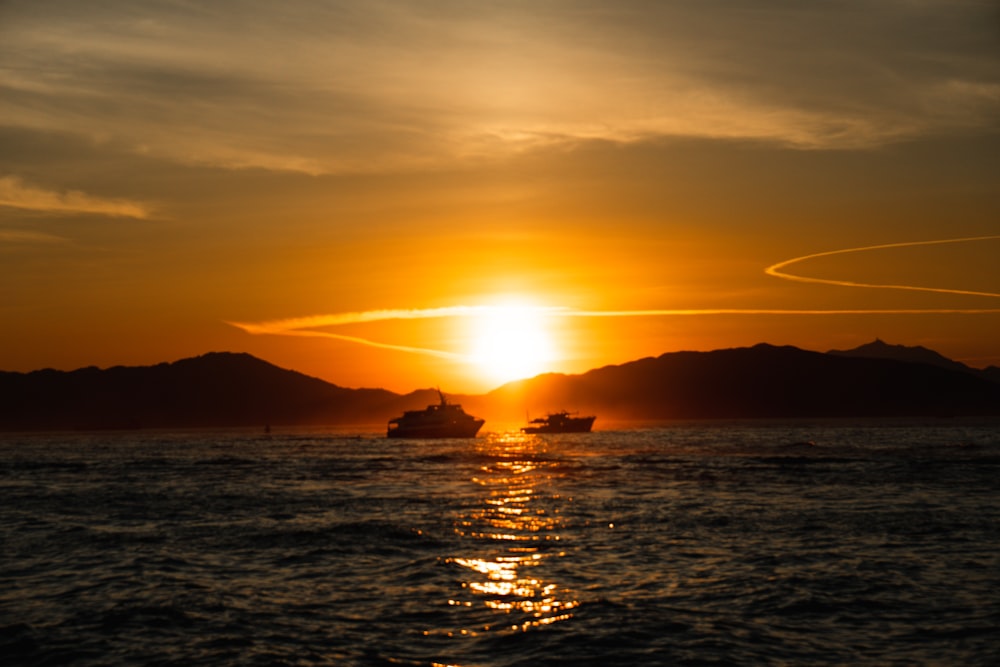 un coucher de soleil sur un plan d’eau avec un bateau au loin