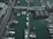 An aerial view of a marina with multiple boats and yachts docked alongside wooden piers. The area includes buildings with modern architecture and a bridge connecting different sections of the marina.