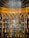 An ornate wooden cabinet with an intricately designed arched pattern housing numerous vintage glass bottles, each labeled and arranged neatly on shelves. A detailed ceiling with a fan-like pattern crowns the cabinet.