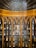 An ornate wooden cabinet with an intricately designed arched pattern housing numerous vintage glass bottles, each labeled and arranged neatly on shelves. A detailed ceiling with a fan-like pattern crowns the cabinet.