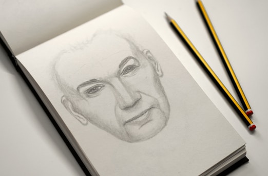 A close-up of Jorge Sierra's hand sketching a detailed self-portrait in a notebook.