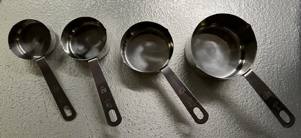 A set of stainless steel measuring cups and spoons with fresh herbs in the background