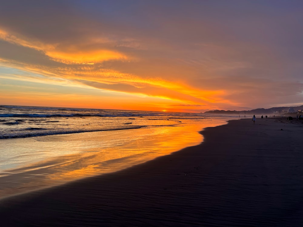 a sunset on a beach with people walking on the beach