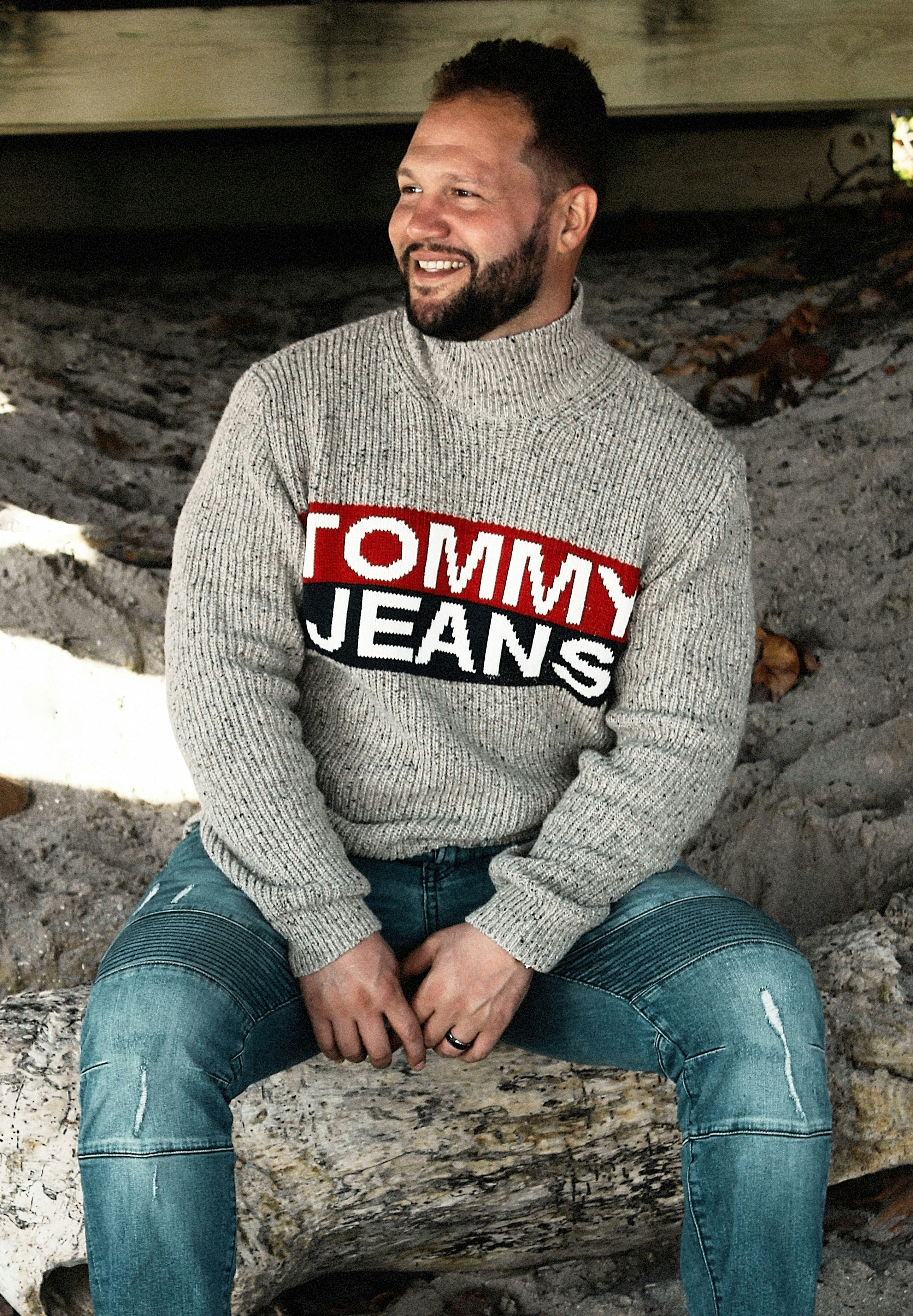 a man sitting on a log wearing a tommy jeans sweater