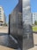 A black granite monument with the title 'Columbia River Watershed' engraved on its surface along with the names of contributors. Water flows gently down one side of the monument. Surrounding the monument are modern buildings with glass windows and greenery in a park-like setting.