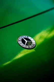 Close-up of a Mercedes emblem shining on a glossy black hood with golden reflections