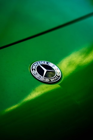 Close-up of a Mercedes emblem shining on a glossy black hood with golden reflections