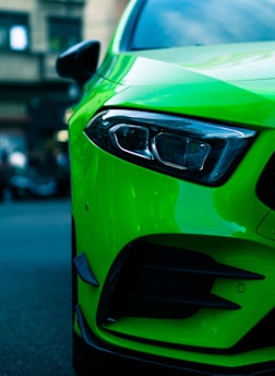 A vibrant green sports car with a sleek design is parked on the street. The focus is on the front headlight and the aerodynamic lines of the vehicle.