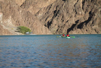 A serene river with kayakers paddling near rocky cliffs under a bright blue sky.