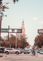 A busy urban street scene with multiple cars and a bicyclist at the intersection of N Miami Ave. A tall, ornate building is visible in the background with trees lining the streets.