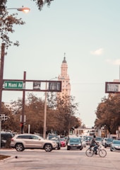 A busy urban street scene with multiple cars and a bicyclist at the intersection of N Miami Ave. A tall, ornate building is visible in the background with trees lining the streets.