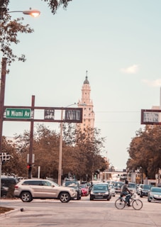 A busy urban street scene with multiple cars and a bicyclist at the intersection of N Miami Ave. A tall, ornate building is visible in the background with trees lining the streets.