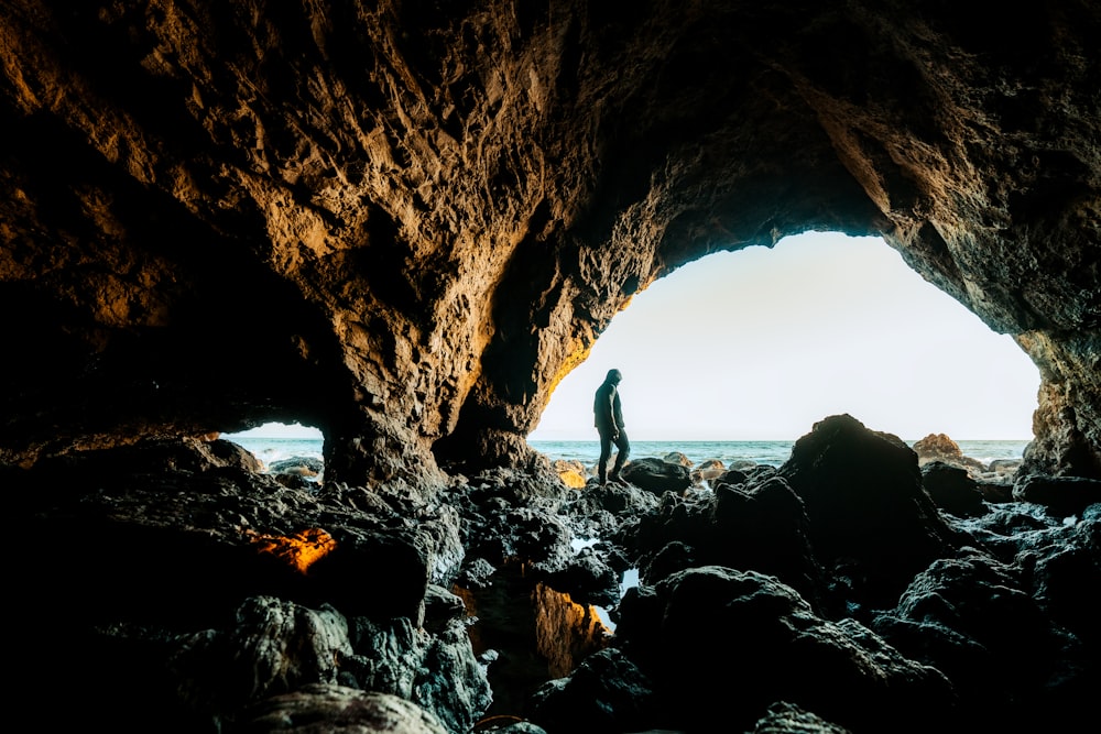 a man standing inside of a cave next to the ocean