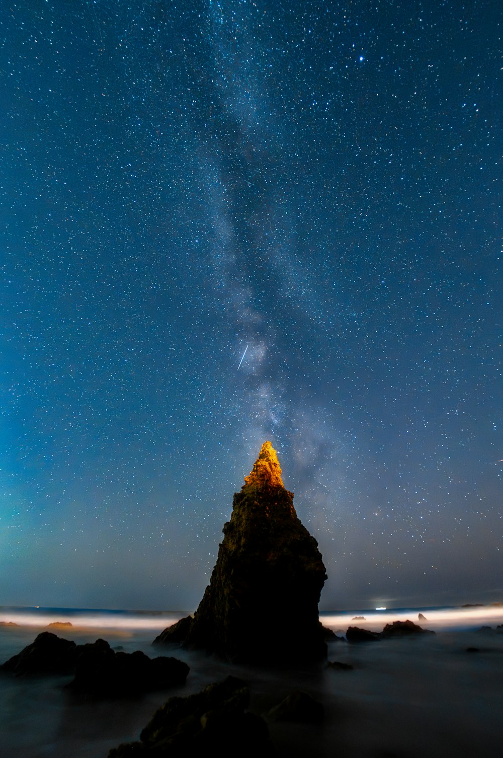 the night sky with stars above a rocky outcropping