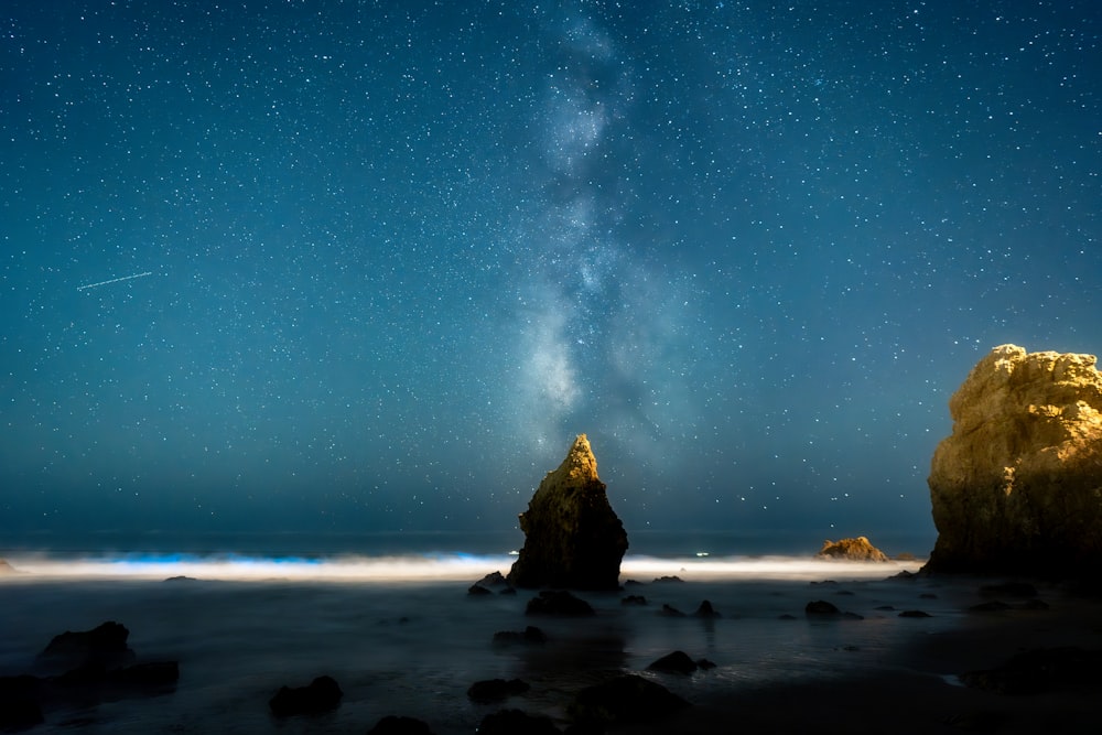 a night sky filled with stars above a rocky beach