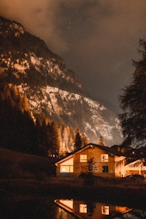 Nighttime exterior of a minimalist mountain lodge illuminated by warm interior lighting.