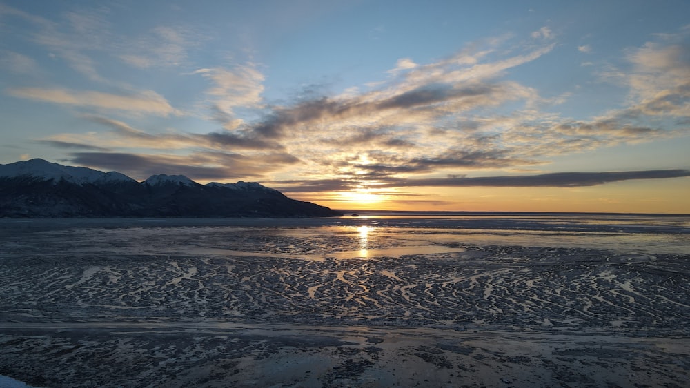 the sun is setting over the ocean with mountains in the background