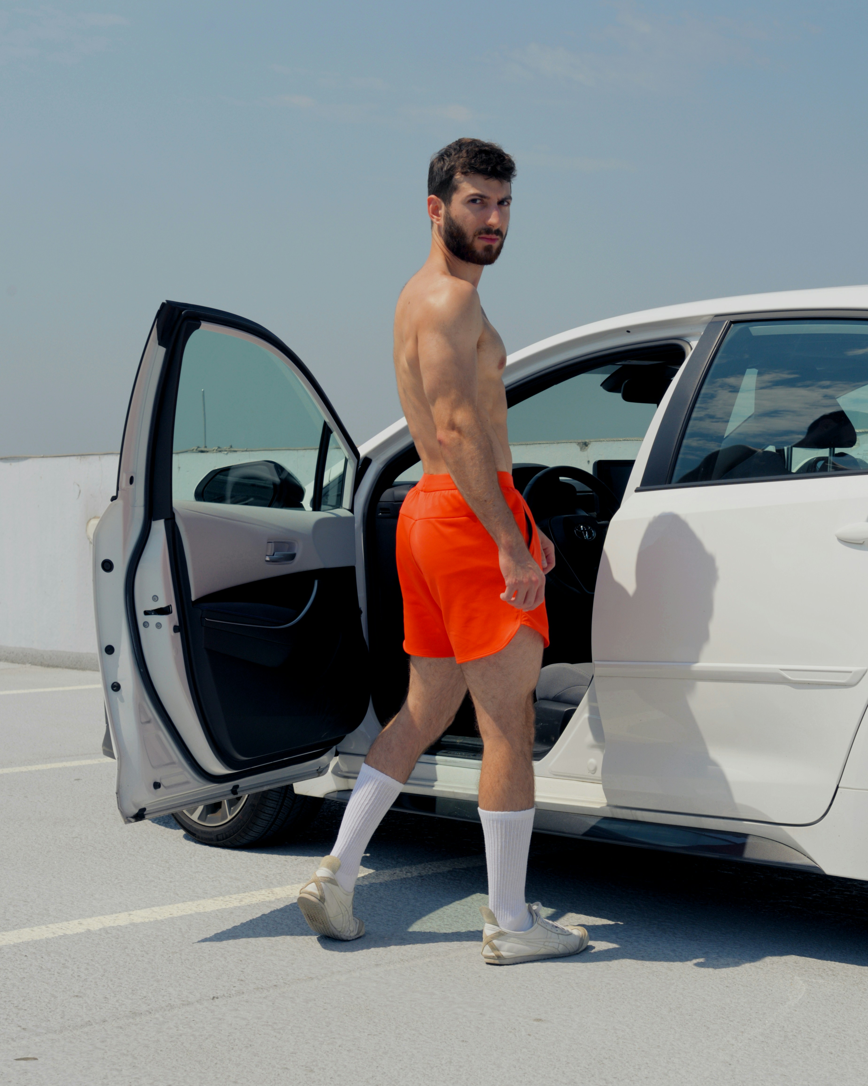 A man in orange shorts stepping out of a white car photo Free Image