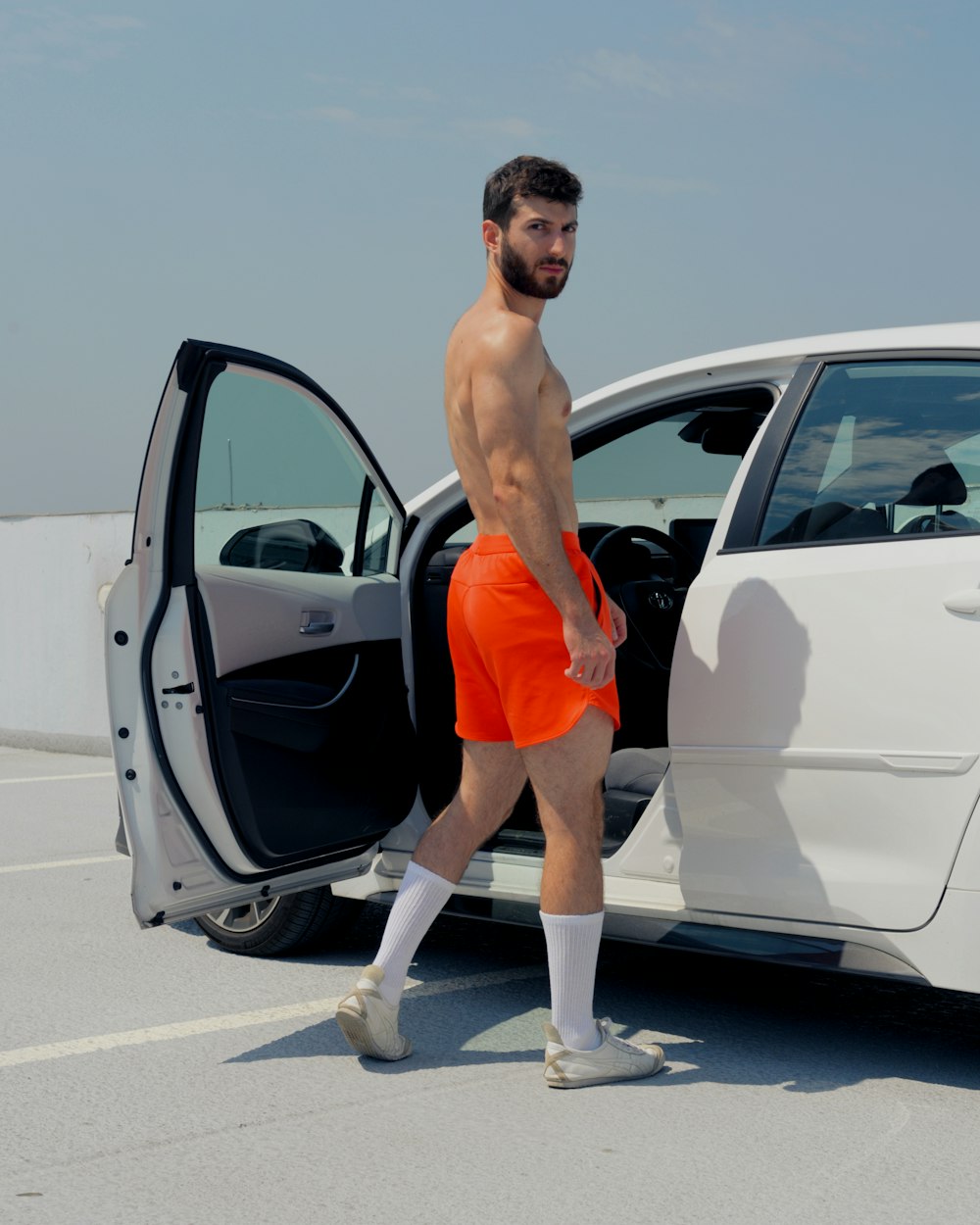 a man in orange shorts stepping out of a white car