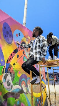 Children painting a vibrant mural under a bright sky.