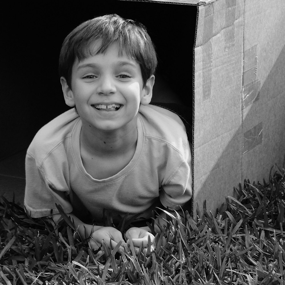 a young boy laying in a cardboard box on the grass
