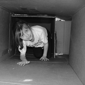 A baby happily playing inside a cardboard box surrounded by smaller boxes.