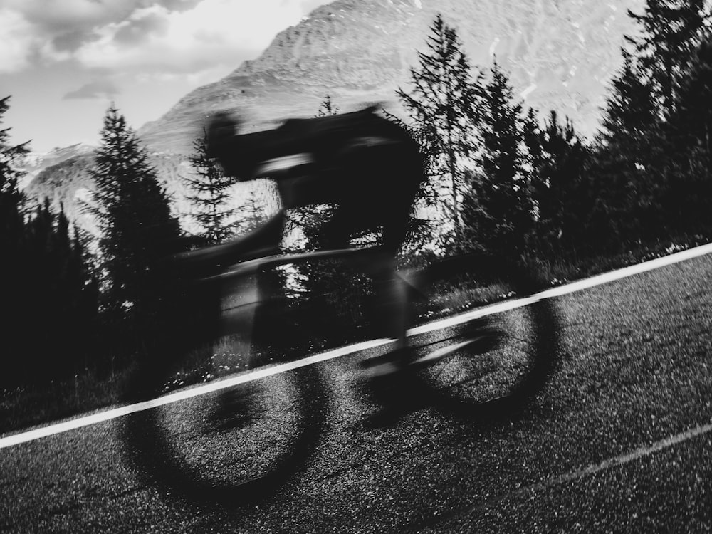 a man riding a bike down a road next to a forest